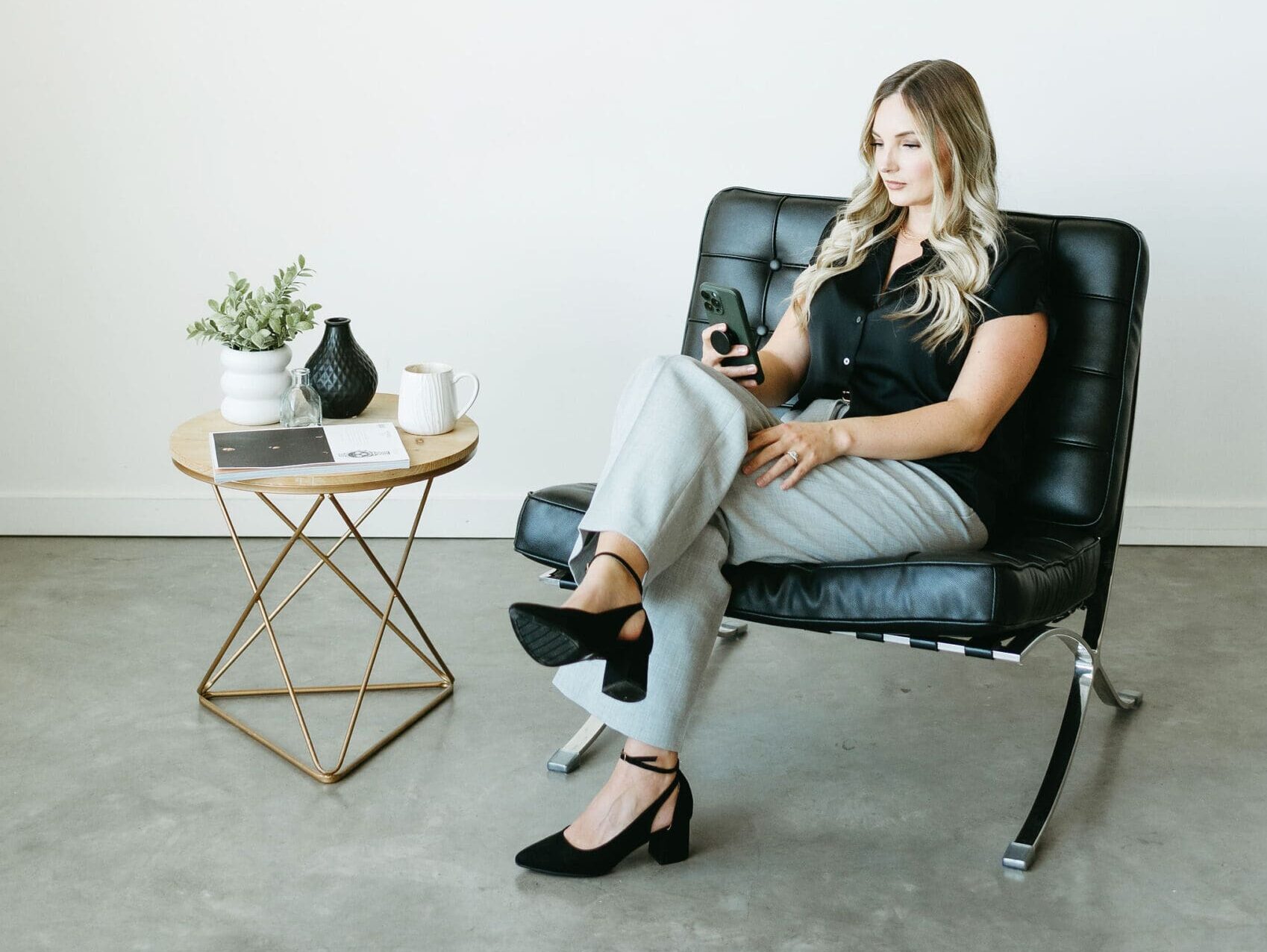 Karly Whitaker sits in leather chair on her phone, scrolling the HoneyBook app that offers a great client experience.