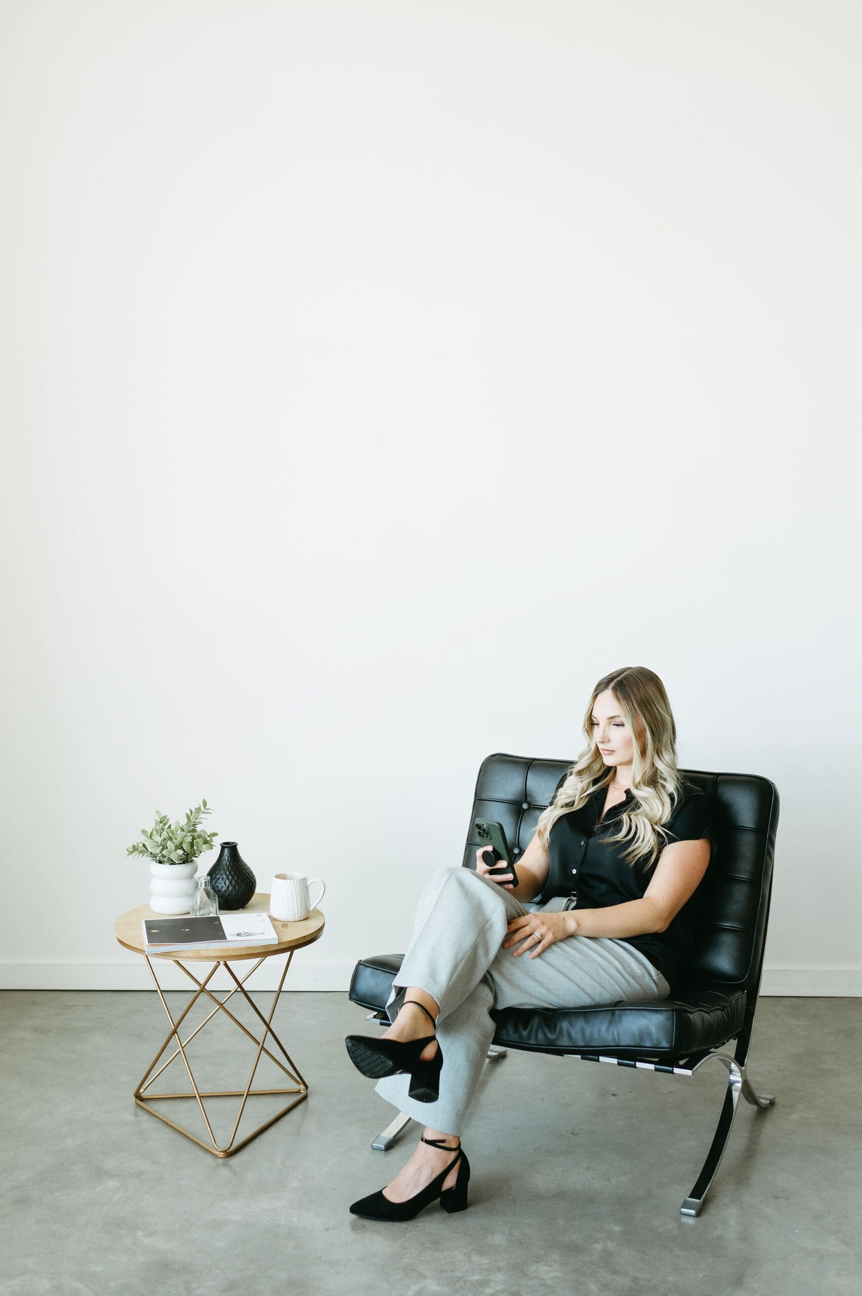 Karly Whitaker sits in leather chair on her phone, scrolling the HoneyBook app that offers a great client experience.