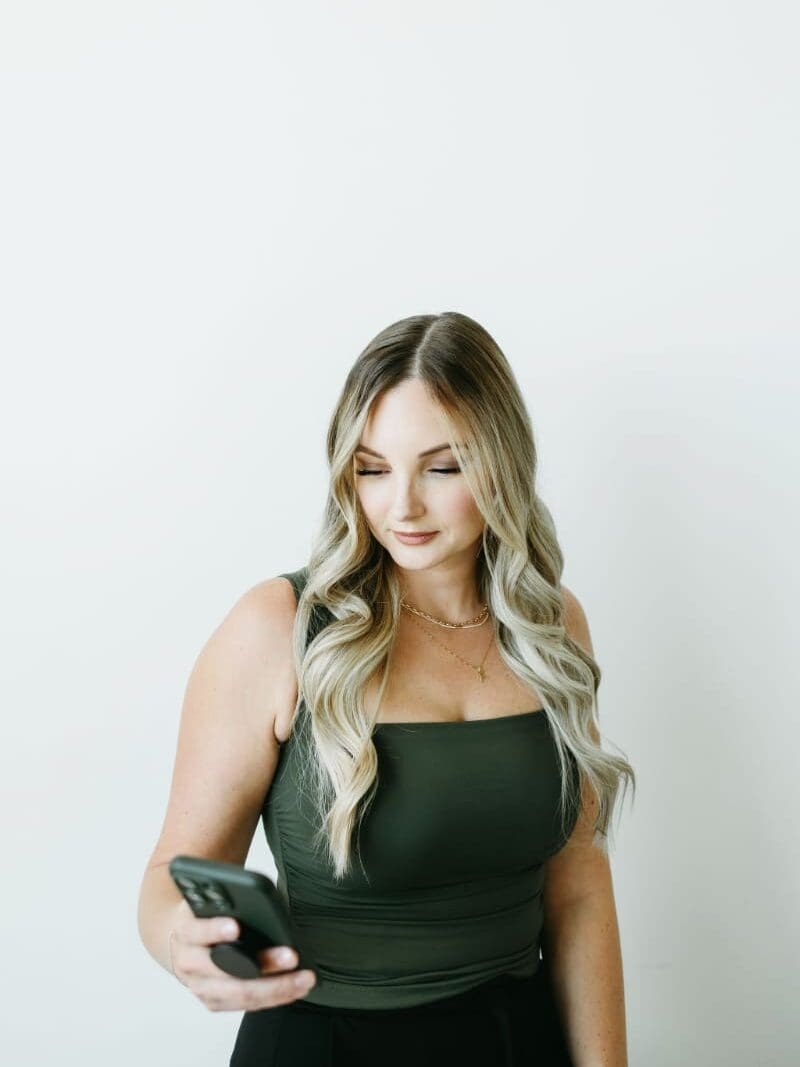 Woman in green top looking at phone with soft expression.