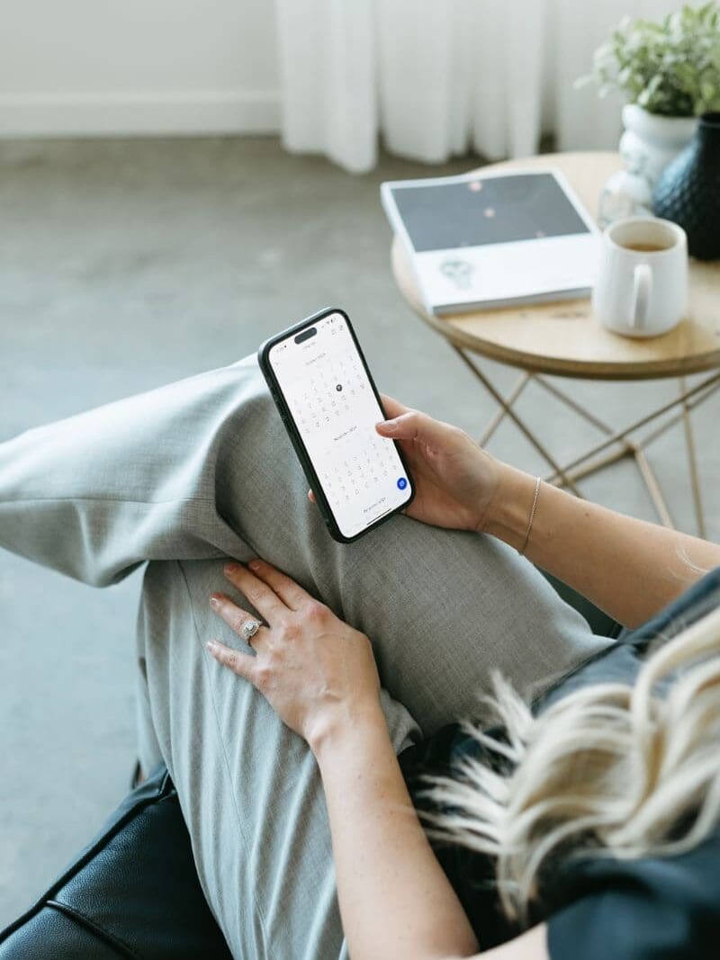 Woman checking calendar app on iPhone while sitting in a modern workspace. Ideal setting for reviewing HoneyBook updates on the go.