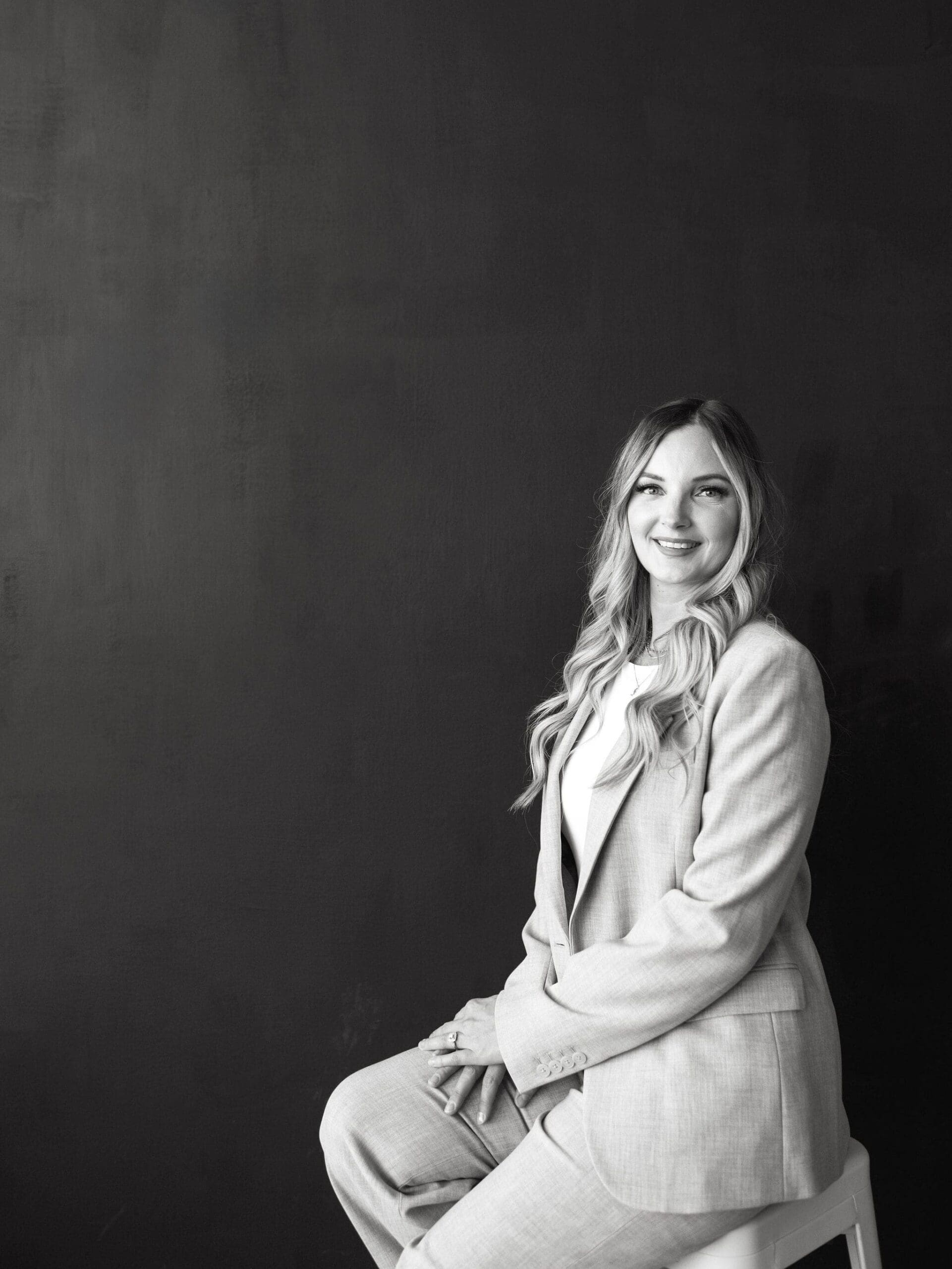 Business consultant seated on a stool against a dark backdrop, wearing a light suit and smiling confidently, representing a professional HoneyBook expert and client workflow strategist. | honeybook lead forms