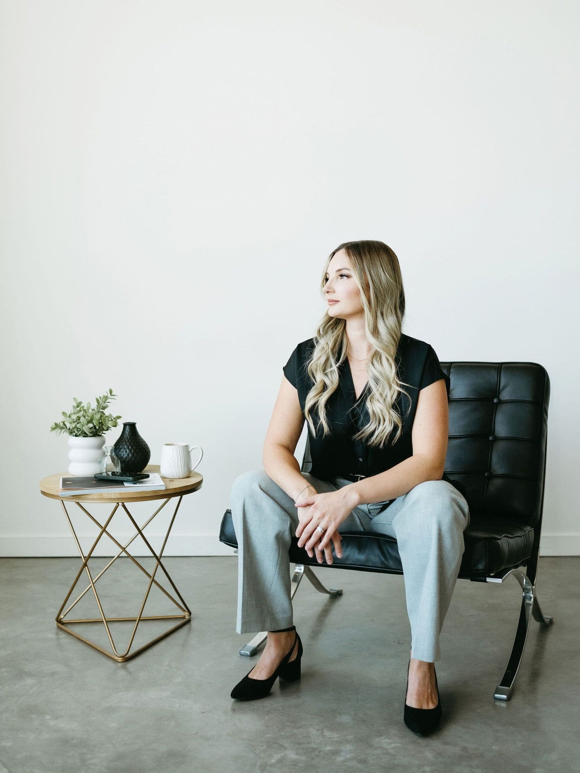Creative business consultant seated in a modern chair with a minimal workspace, styled in a professional outfit, reflecting organized systems and HoneyBook lead form strategy.