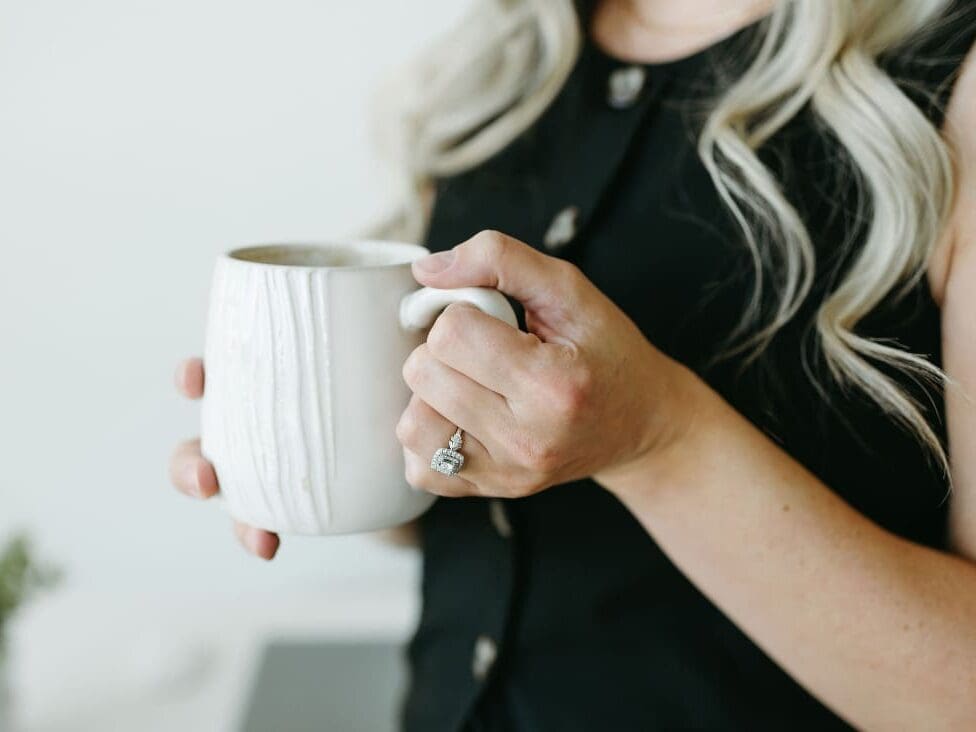 Close-up of HoneyBook consultant Karly Whitaker holding a coffee mug, showing engagement ring and neutral professional styling.