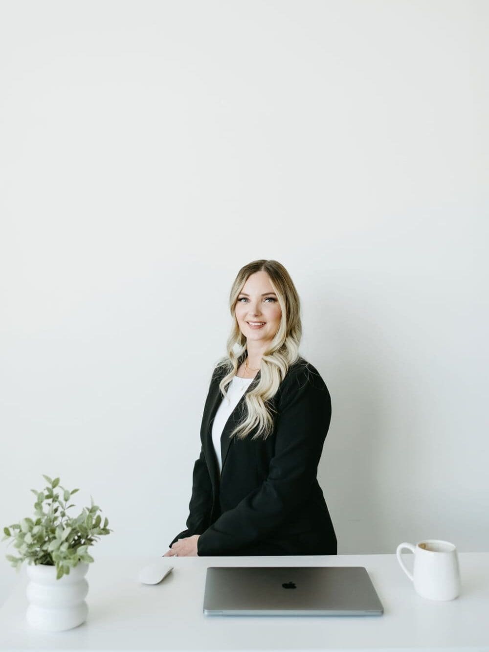 HoneyBook pro Karly Whitaker seated at a clean desk with laptop and coffee, representing an organized backend and streamlined client onboarding experience for service-based business owners.