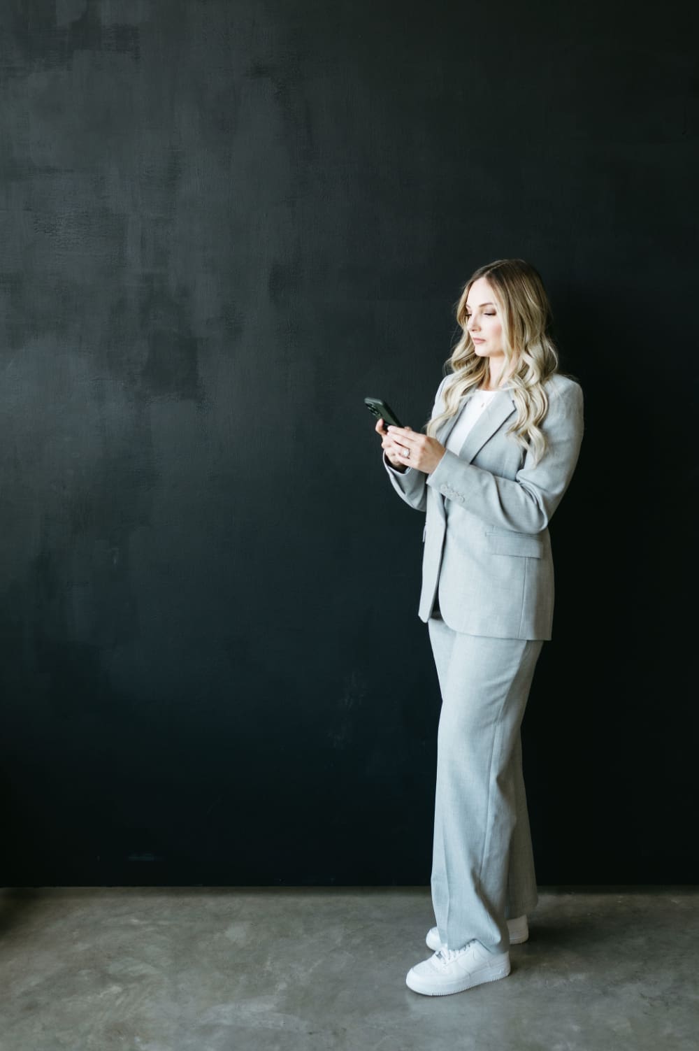 Business owner in a modern suit checking her phone, representing managing inquiries and staying on top of client onboarding and workflows in a streamlined system.