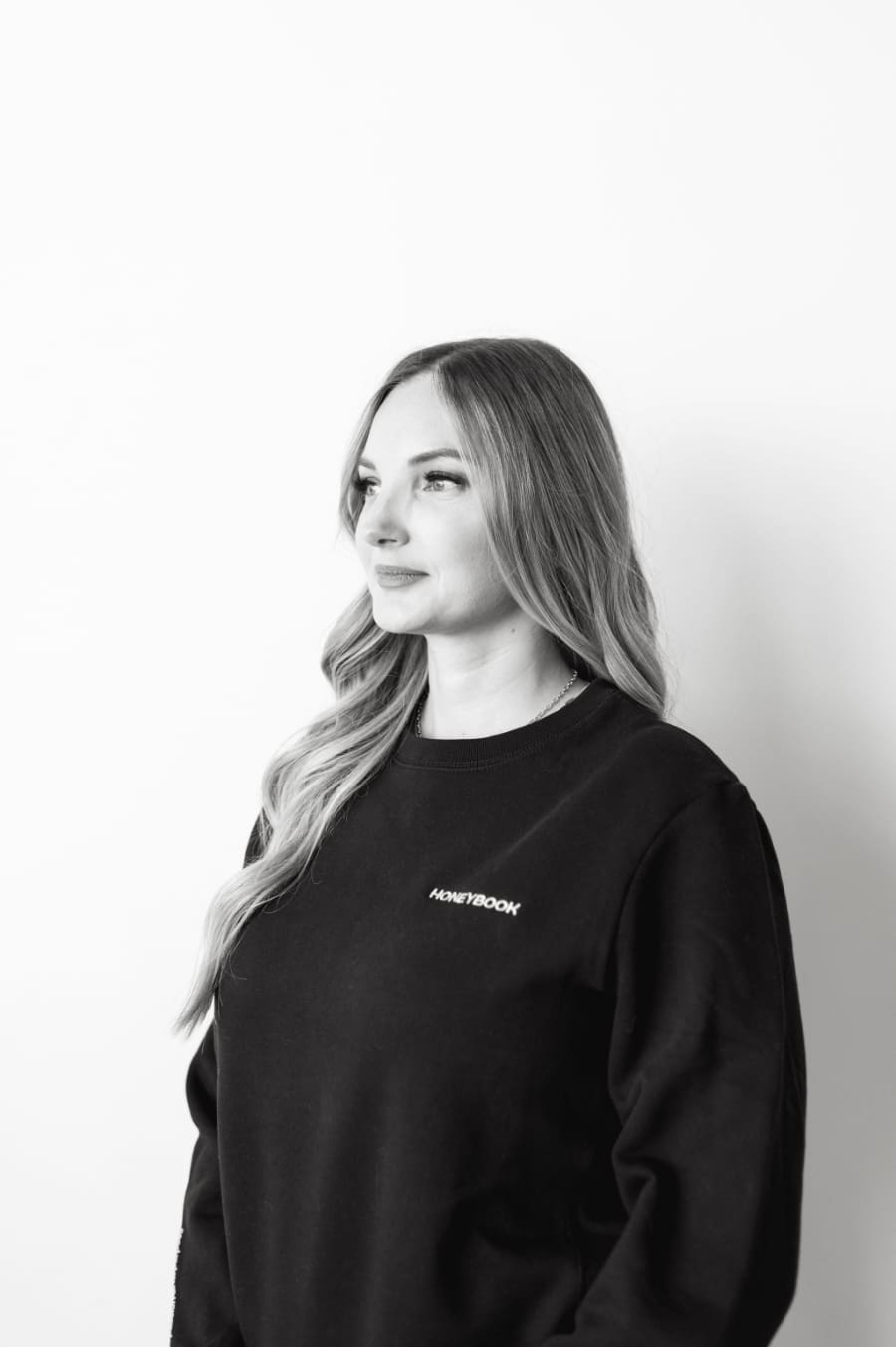 Professional black and white portrait of a HoneyBook consultant wearing a HoneyBook sweatshirt, representing expertise in CRM setup and client systems for creative entrepreneurs.