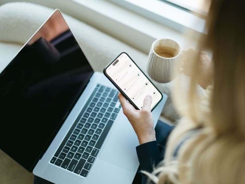 Close-up of a business owner using HoneyBook on a phone next to a laptop, illustrating client communication, workflows, and automation in a dubsado vs honeybook discussion.