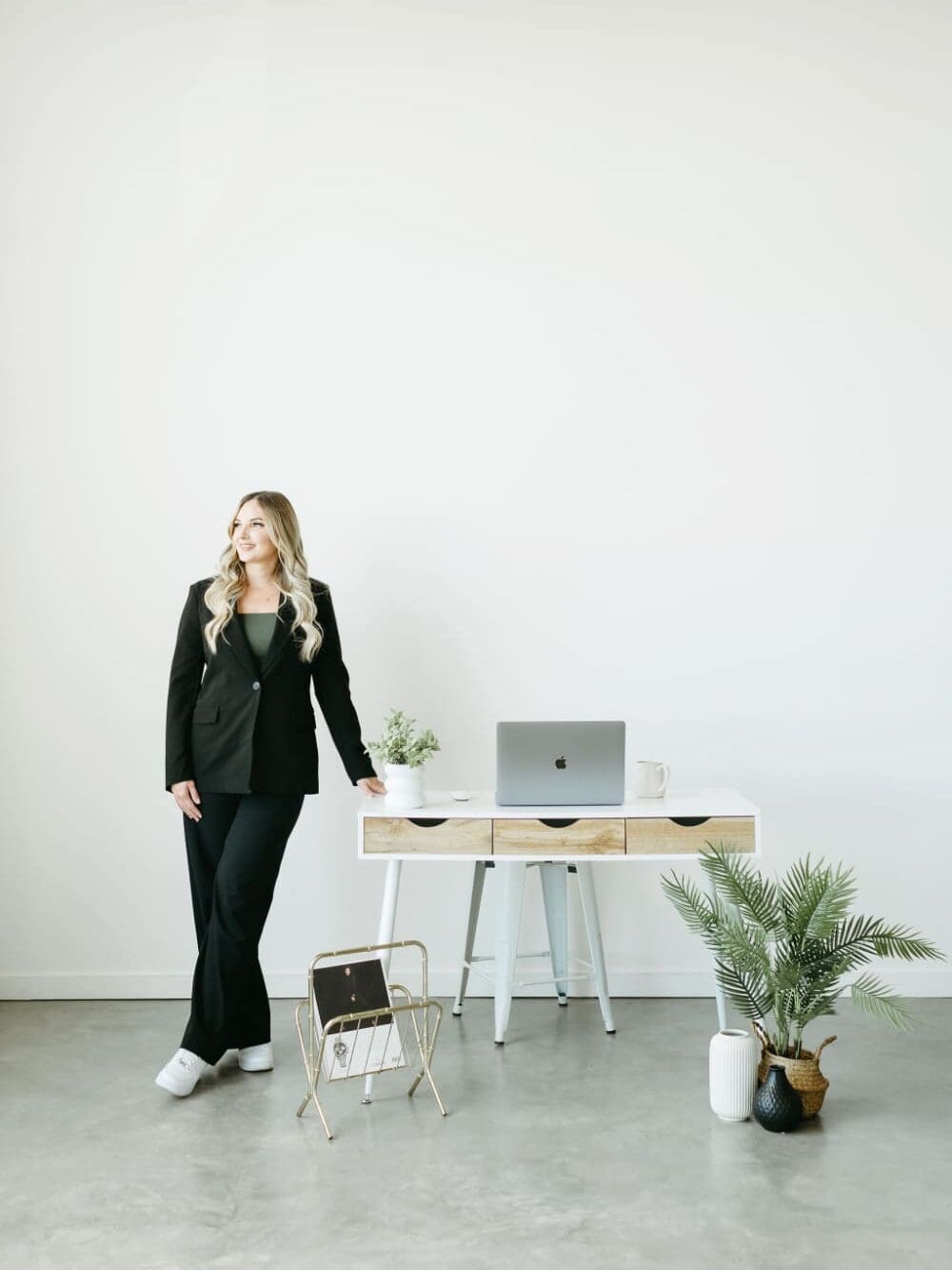 Karly Whitaker, Certified HoneyBook Pro, standing beside a modern white desk with a laptop, ready to help creative entrepreneurs choose between HoneyBook vs 17hats.