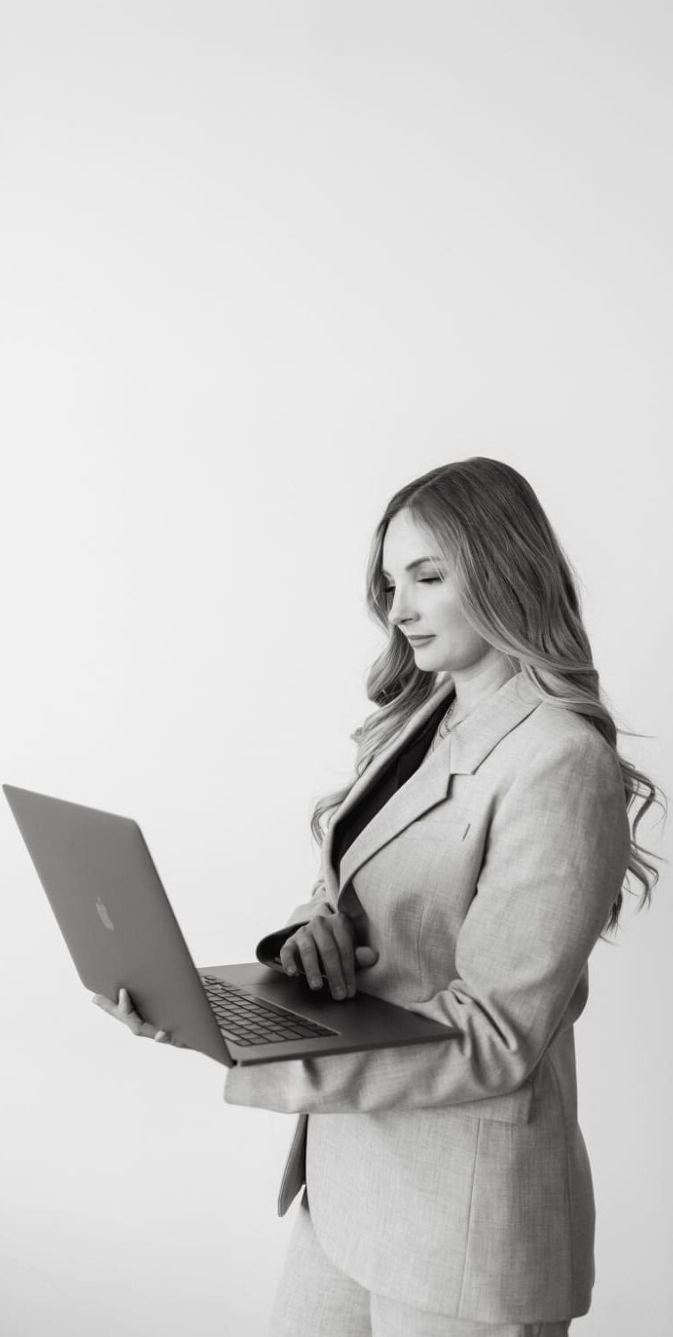 Black and white photo of Karly Whitaker, HoneyBook Pro and consultant, holding a laptop.