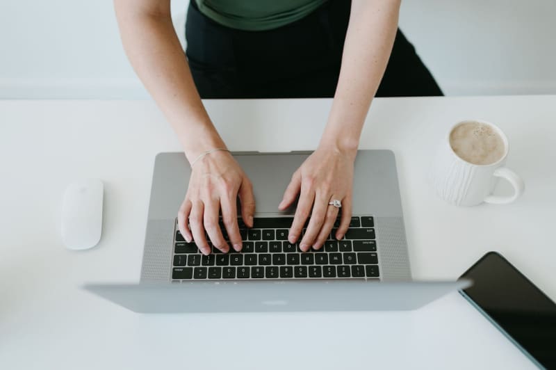 Overhead view of hands typing on a laptop with coffee nearby, working through a HoneyBook and QuickBooks setup to streamline invoicing, payments, and bookkeeping for a creative business.
