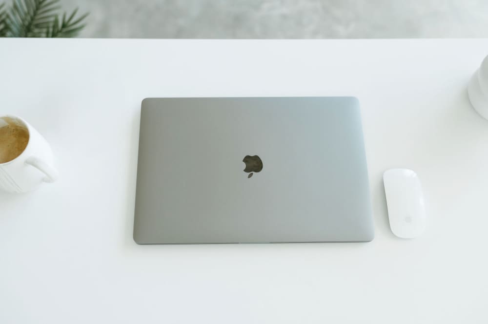 Minimal white workspace featuring a laptop, coffee, and mouse, representing business automation and using Zapier with HoneyBook to streamline client workflows.