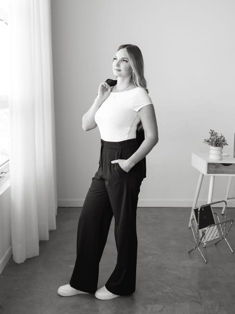 Black-and-white portrait of a business owner standing beside a bright window in a modern office, representing the personal service and professional experience behind a thoughtful HoneyBook proposal.