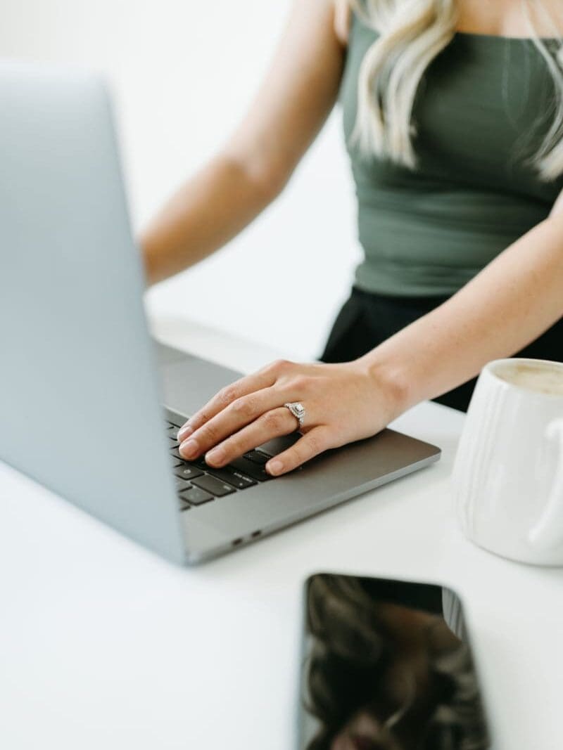 Business owner working on a laptop with coffee and phone nearby, using the HoneyBook scheduler to manage client bookings, availability, and scheduling from one place.