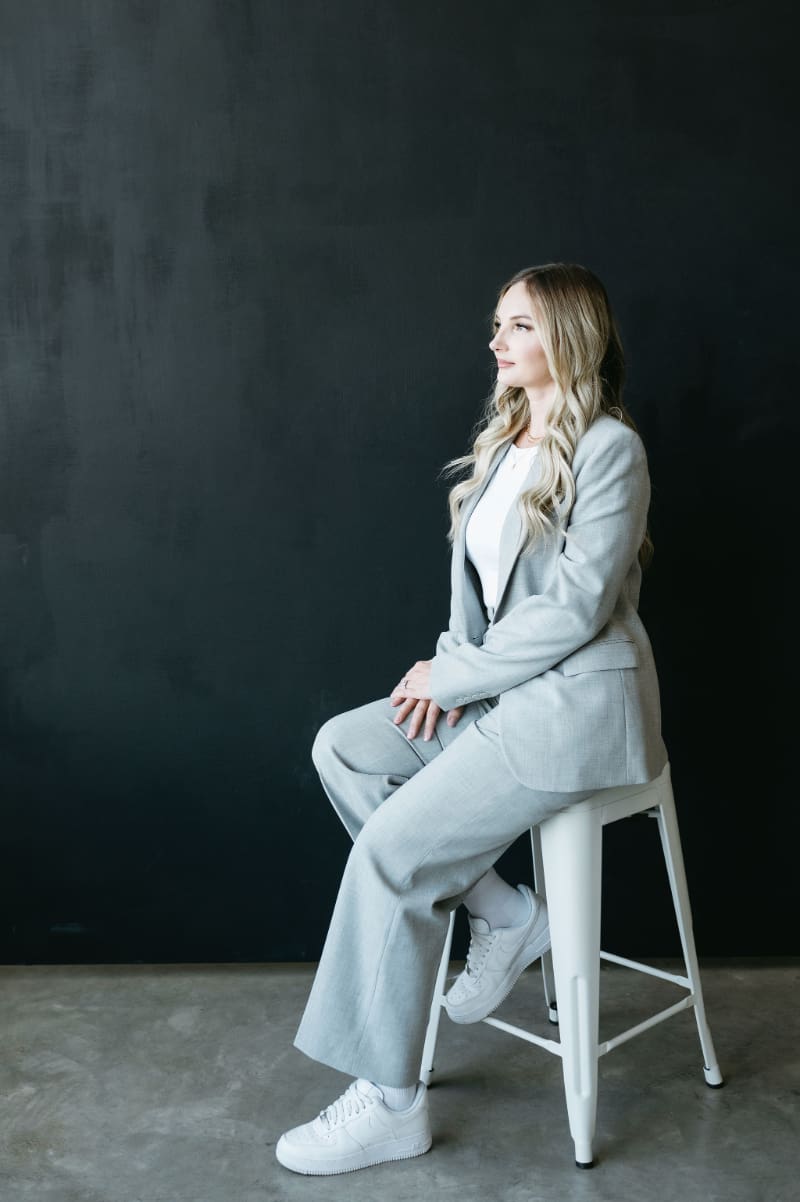 HoneyBook Pro Karly sitting in a light grey suit against a dark backdrop, helping creative entrepreneurs use HoneyBook email templates to simplify client communication.