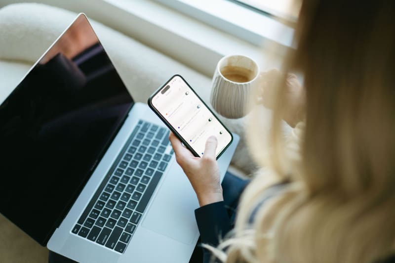 Creative business owner checking her phone beside a laptop while managing HoneyBook pipelines