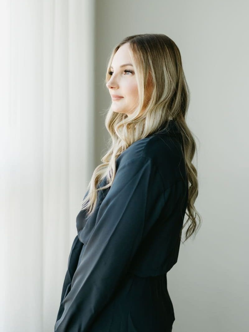 Side-profile branding portrait of HoneyBook consultant Karly Whitaker wearing a dark blouse, with long blonde waves and soft natural window light. Her blog explains how multiple project dates in HoneyBook help organize client events and appointments.